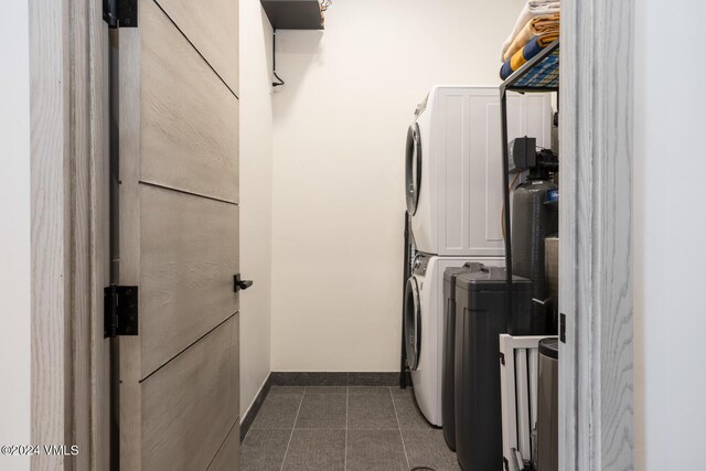 clothes washing area featuring stacked washer and clothes dryer and dark tile patterned floors