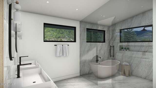 bathroom with marble finish floor, tile walls, a sink, and a soaking tub