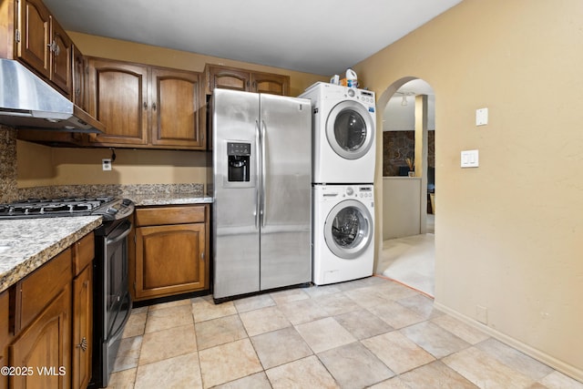 laundry area featuring laundry area, arched walkways, and stacked washing maching and dryer