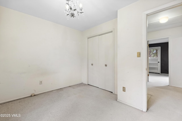 unfurnished bedroom featuring carpet flooring, baseboards, a notable chandelier, and a closet
