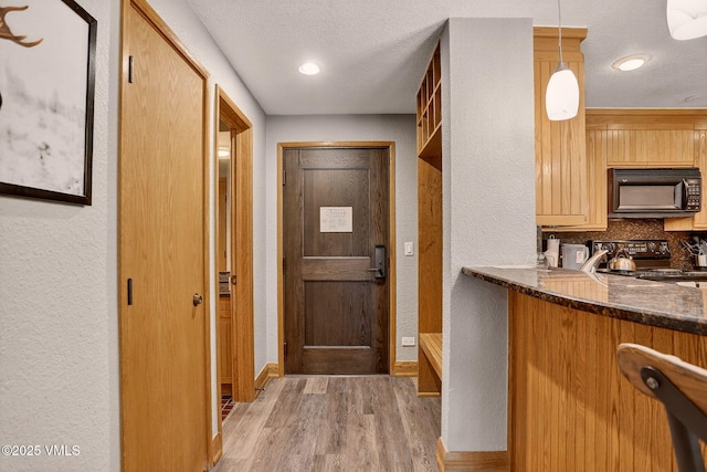 120 Offerson Unit 5160, Beaver Creek, CO 81620 - kitchen featuring black appliances, a textured wall, light wood-style flooring, backsplash, and dark stone countertops