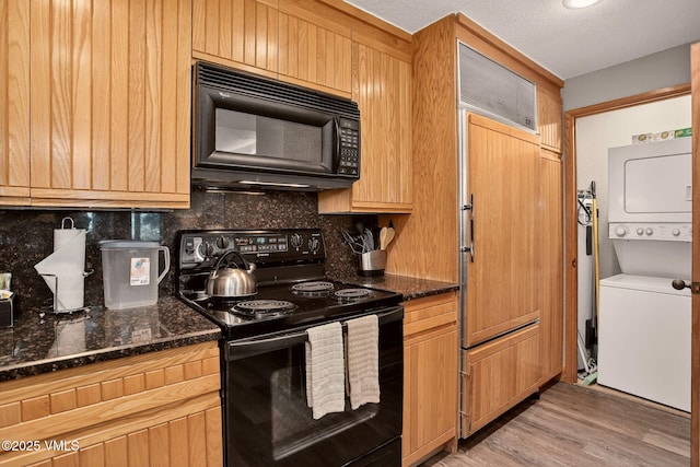 120 Offerson Unit 5160, Beaver Creek, CO 81620 - kitchen with black appliances, stacked washing machine and dryer, decorative backsplash, light wood-type flooring, and dark stone counters
