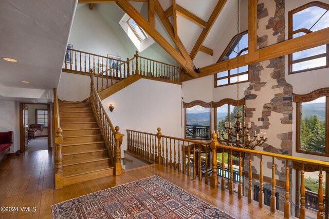 staircase with wood-type flooring, beam ceiling, a skylight, and high vaulted ceiling