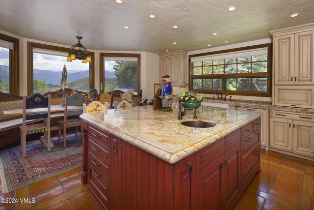 kitchen featuring an island with sink, hanging light fixtures, a mountain view, a healthy amount of sunlight, and cream cabinetry