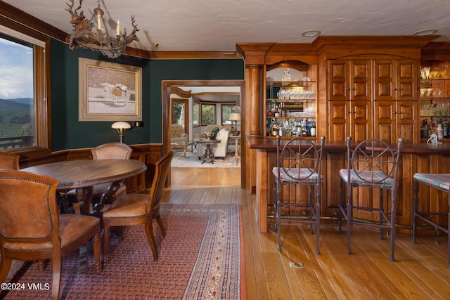 dining area with indoor bar, crown molding, a chandelier, and light wood-type flooring