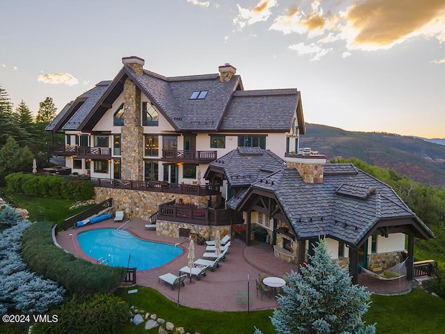 back house at dusk featuring a balcony, a covered pool, a patio, and a lawn