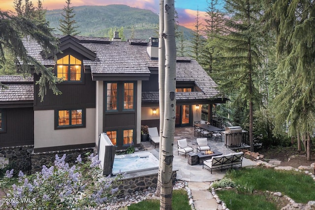 416 Forest Rd Unit A, Vail, CO 81657 - back of house at dusk featuring a balcony, a patio area, an outdoor living space with a fire pit, a mountain view, and an outdoor hot tub