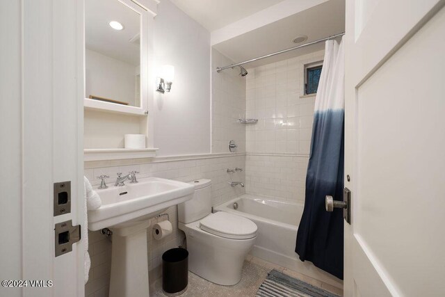 full bathroom with sink, shower / bath combo, tile walls, tile patterned floors, and toilet