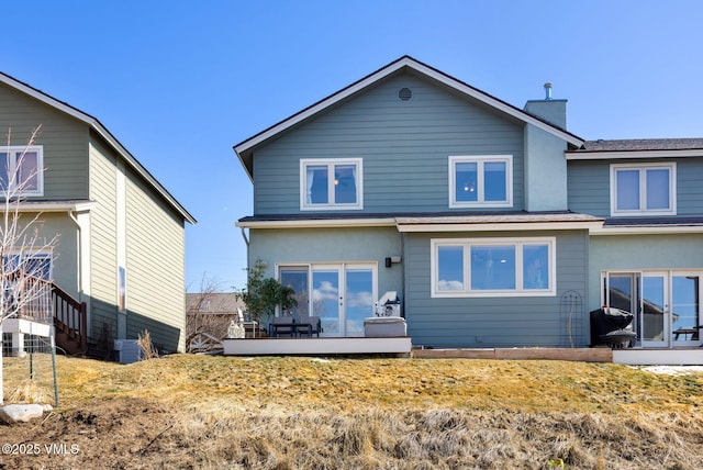 back of property with a deck, stucco siding, french doors, and a chimney