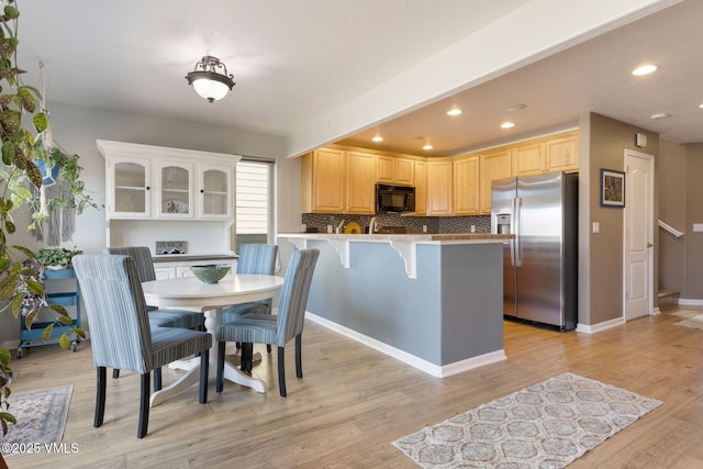 kitchen featuring light brown cabinets, a peninsula, stainless steel refrigerator with ice dispenser, black microwave, and backsplash