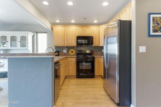 kitchen with a sink, black appliances, light brown cabinetry, and light wood finished floors