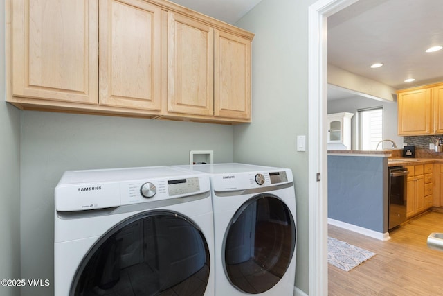 washroom with cabinet space, recessed lighting, a sink, washing machine and dryer, and light wood-type flooring