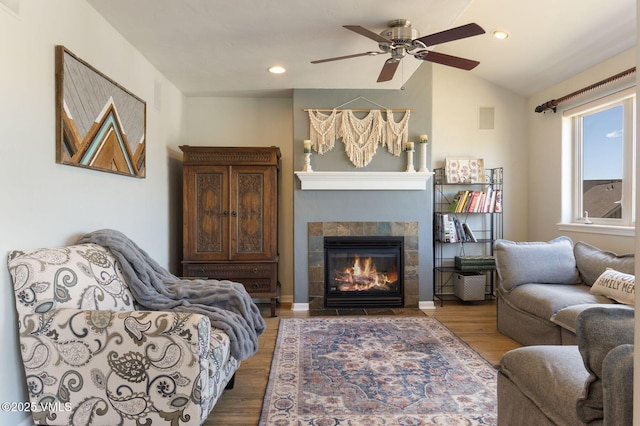 living area with a fireplace, vaulted ceiling, wood finished floors, and a ceiling fan