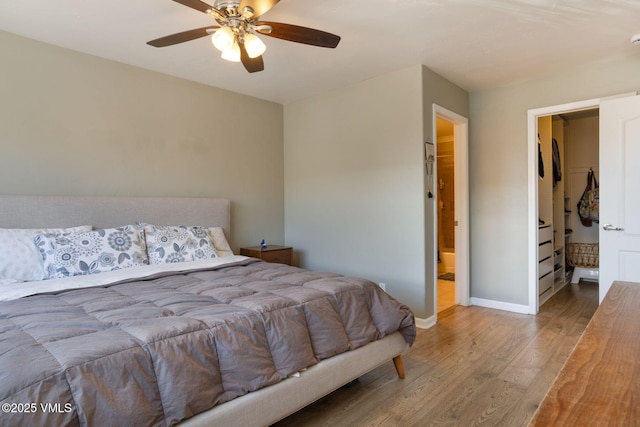 bedroom with a ceiling fan, a walk in closet, baseboards, and wood finished floors