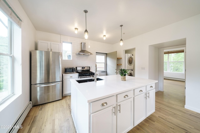 511 Metcalf Unit J30, Avon, CO 81620 - kitchen with stainless steel appliances, estacked washer and dryer, a sink, a baseboard radiator, and wall chimney range hood