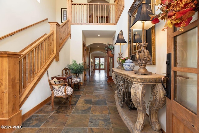 entryway featuring baseboards, stairs, stone tile floors, a high ceiling, and arched walkways