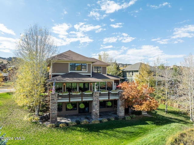 back of house featuring a patio, a lawn, and roof with shingles