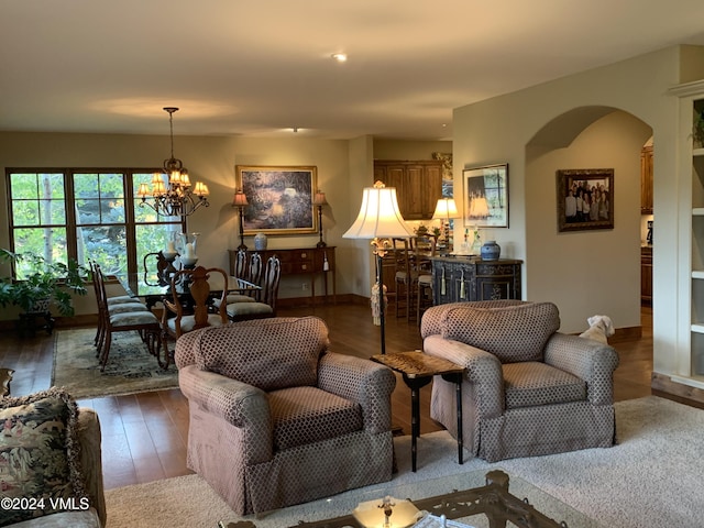 living room with arched walkways, an inviting chandelier, and wood finished floors