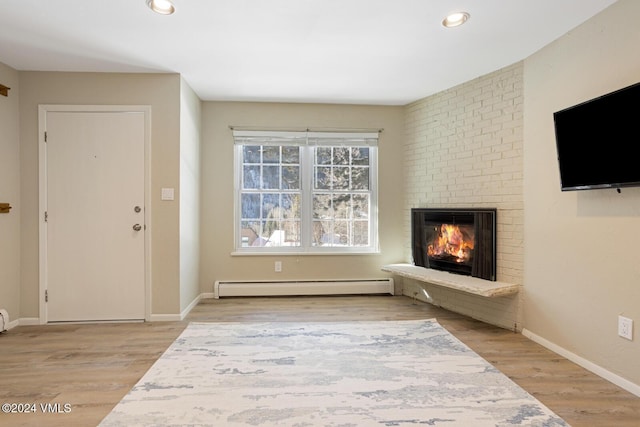 interior space featuring a brick fireplace, a baseboard heating unit, and light hardwood / wood-style floors