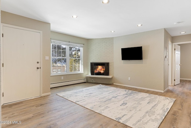 unfurnished living room featuring baseboard heating, a fireplace, and light wood-type flooring