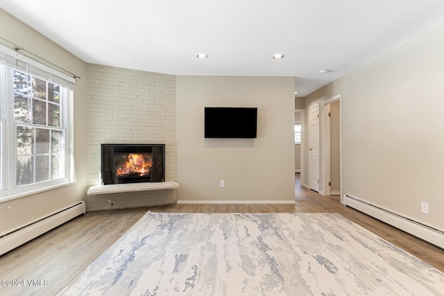 unfurnished living room with a baseboard heating unit, a fireplace, and light hardwood / wood-style floors