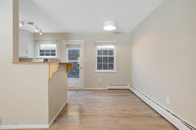 unfurnished dining area featuring a baseboard radiator, rail lighting, and light hardwood / wood-style flooring