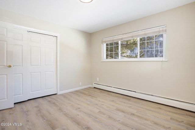 unfurnished bedroom with baseboard heating, a closet, and light wood-type flooring