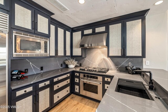 130 Daybreak Rd Unit R401, Beaver Creek, CO 81620 - kitchen featuring appliances with stainless steel finishes, exhaust hood, a sink, tasteful backsplash, and light wood-style flooring