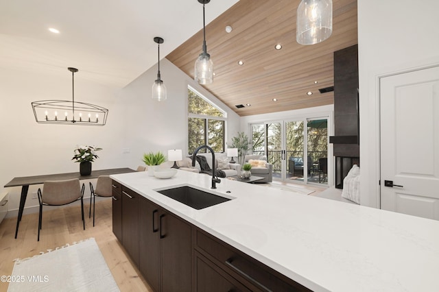 kitchen with pendant lighting, light wood-style flooring, a sink, dark brown cabinetry, and light countertops