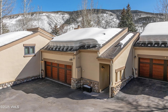 exterior space featuring an attached garage, aphalt driveway, stucco siding, stone siding, and a mountain view