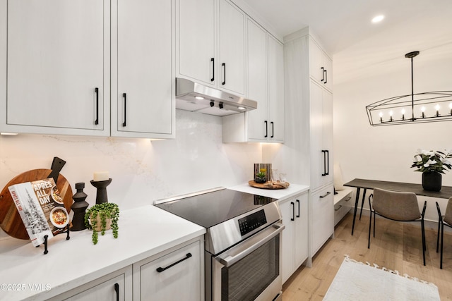 kitchen featuring stainless steel range with electric stovetop, white cabinets, under cabinet range hood, and a chandelier