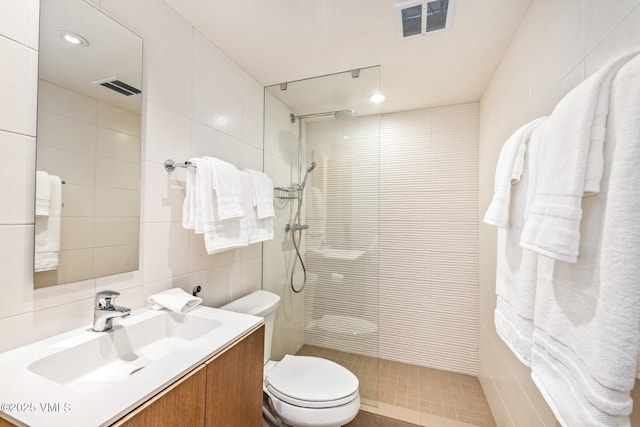 bathroom with vanity, tiled shower, tile walls, and toilet