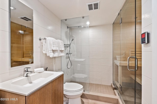 bathroom featuring tasteful backsplash, tile walls, vanity, toilet, and a shower with door