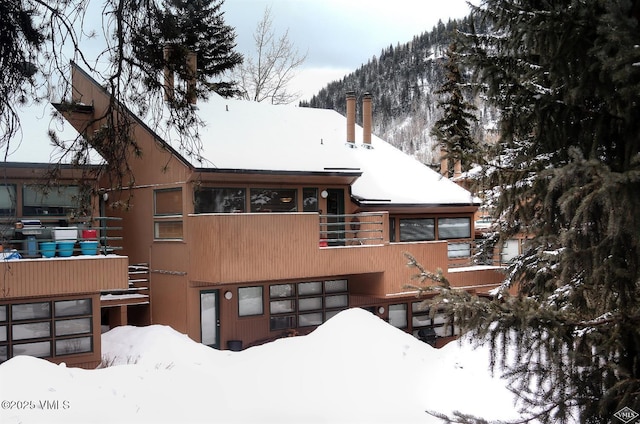 snow covered property featuring a balcony, a chimney, and a garage