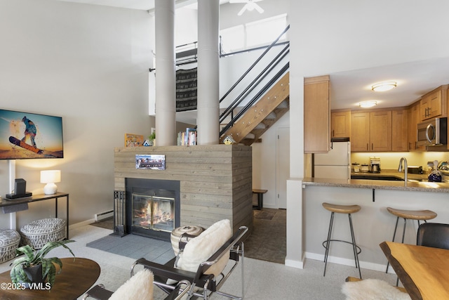 living area with a fireplace with flush hearth, a baseboard heating unit, baseboards, a towering ceiling, and stairs