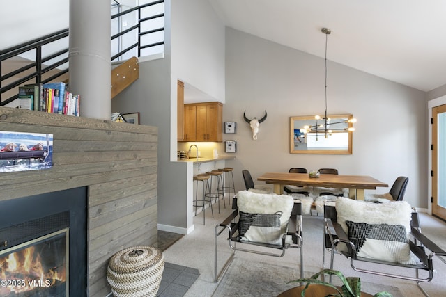 dining room featuring baseboards, high vaulted ceiling, an inviting chandelier, and a glass covered fireplace