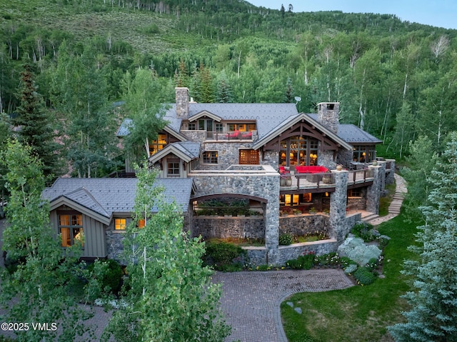 780 Potato Patch Dr, Vail, CO 81657 - back of house with a chimney, a forest view, stone siding, and a balcony
