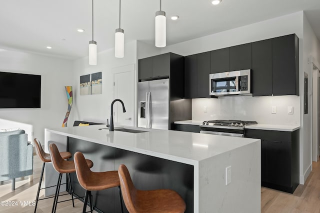 kitchen with pendant lighting, appliances with stainless steel finishes, sink, and a kitchen island with sink