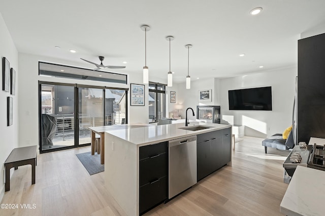 kitchen featuring sink, hanging light fixtures, a kitchen island with sink, stainless steel dishwasher, and light hardwood / wood-style flooring