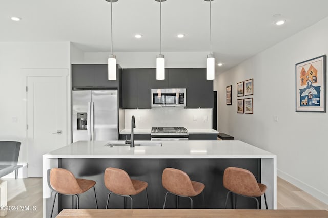 kitchen with sink, light hardwood / wood-style flooring, hanging light fixtures, stainless steel appliances, and a kitchen bar