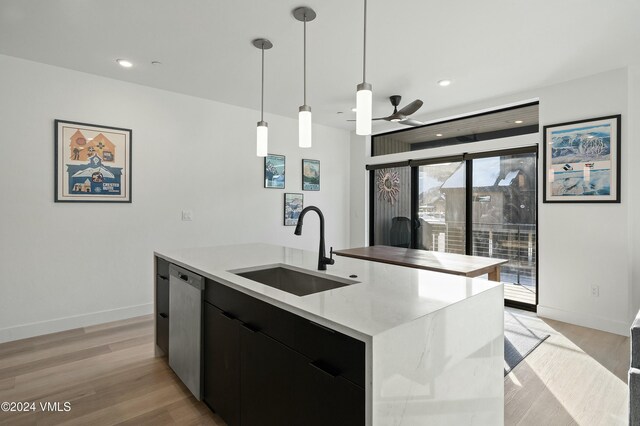 kitchen with an island with sink, dishwasher, sink, hanging light fixtures, and light hardwood / wood-style flooring