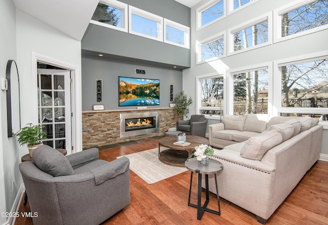 living area with a stone fireplace, wood finished floors, and a towering ceiling