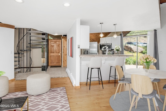 kitchen featuring a kitchen bar, light wood-type flooring, white cabinetry, light countertops, and appliances with stainless steel finishes