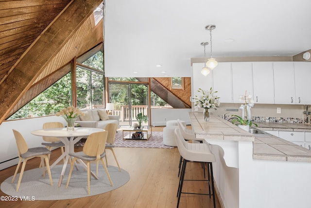 interior space featuring tile counters, a kitchen breakfast bar, light wood-type flooring, white cabinetry, and pendant lighting