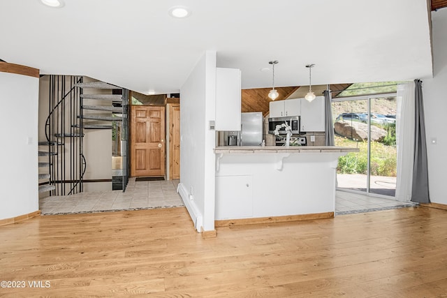 kitchen featuring light wood-style flooring, appliances with stainless steel finishes, light countertops, white cabinetry, and a peninsula
