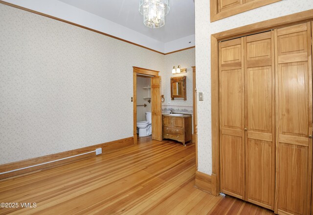 409 Washington St, Eagle, CO 81631 - unfurnished bedroom featuring light wood finished floors, a chandelier, wallpapered walls, a sink, and ensuite bath