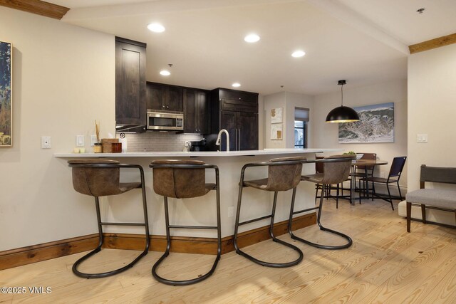 kitchen with kitchen peninsula, a breakfast bar area, decorative backsplash, light hardwood / wood-style floors, and dark brown cabinetry