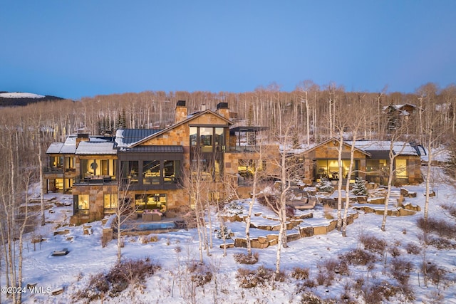 snow covered property featuring stone siding, a chimney, and a balcony