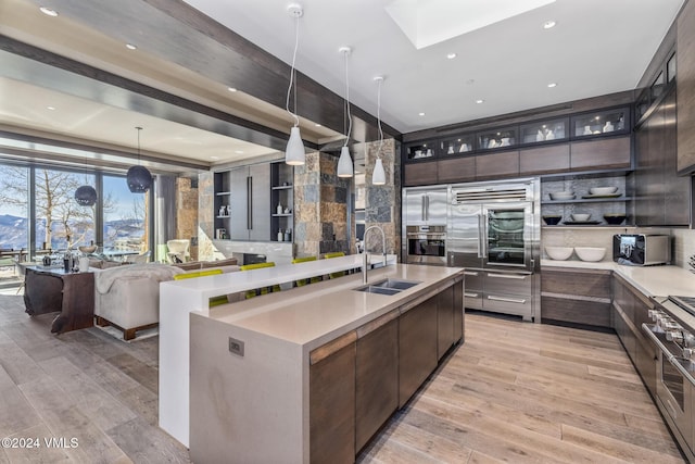 kitchen with a sink, open shelves, light wood-style flooring, and a center island with sink