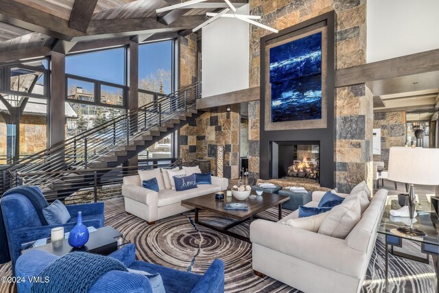 living area featuring beamed ceiling, stairway, a fireplace, and high vaulted ceiling